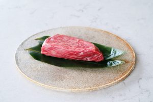 Raw Japanese Wagyu steak with exceptional marbling, served on sasa (bamboo) leaves on a speckled ceramic plate