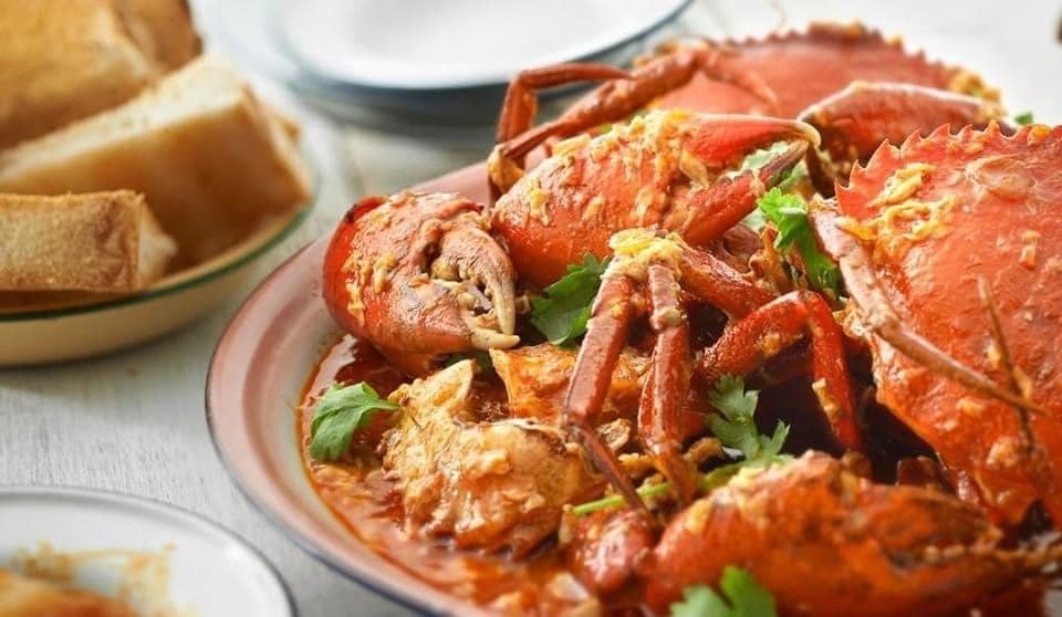 "A large dish of Chili Crab from Aroy-Dee Thai Kitchen, with pieces of crab in a rich red sauce, garnished with cilantro, served with a side of bread or mantou