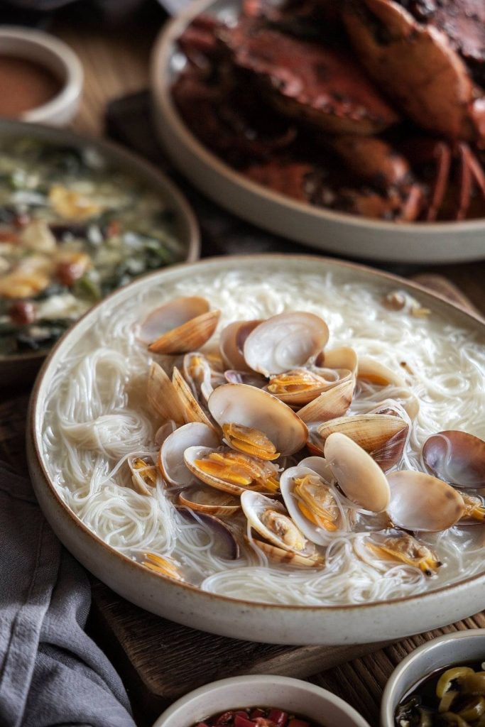A close-up of a large rustic ceramic bowl filled with lala white bee hoon (clams with rice vermicelli noodles) from Diamond Kitchen.