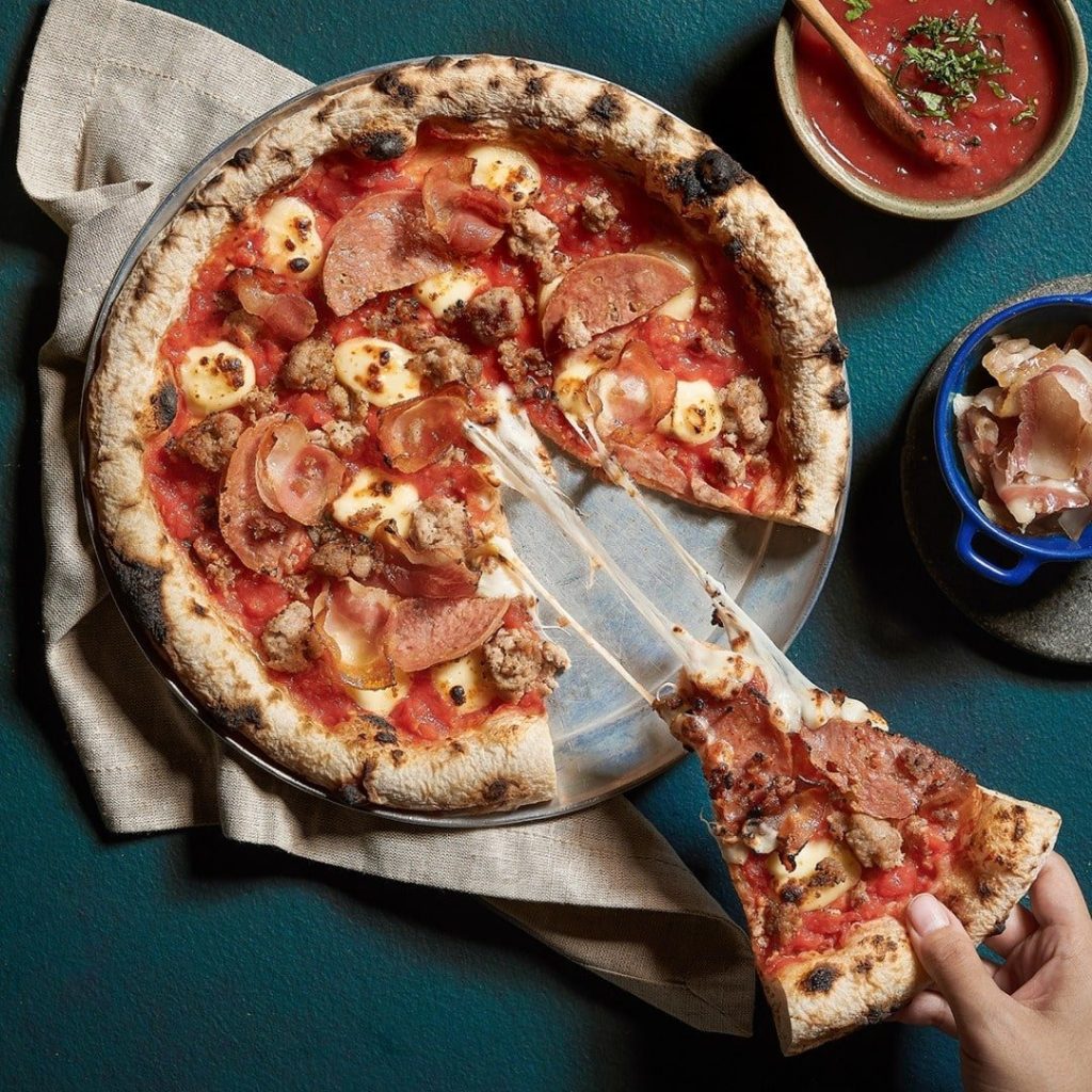 Overhead shot of a meat lover's pizza from Extra Virgin Pizza on a metal pan