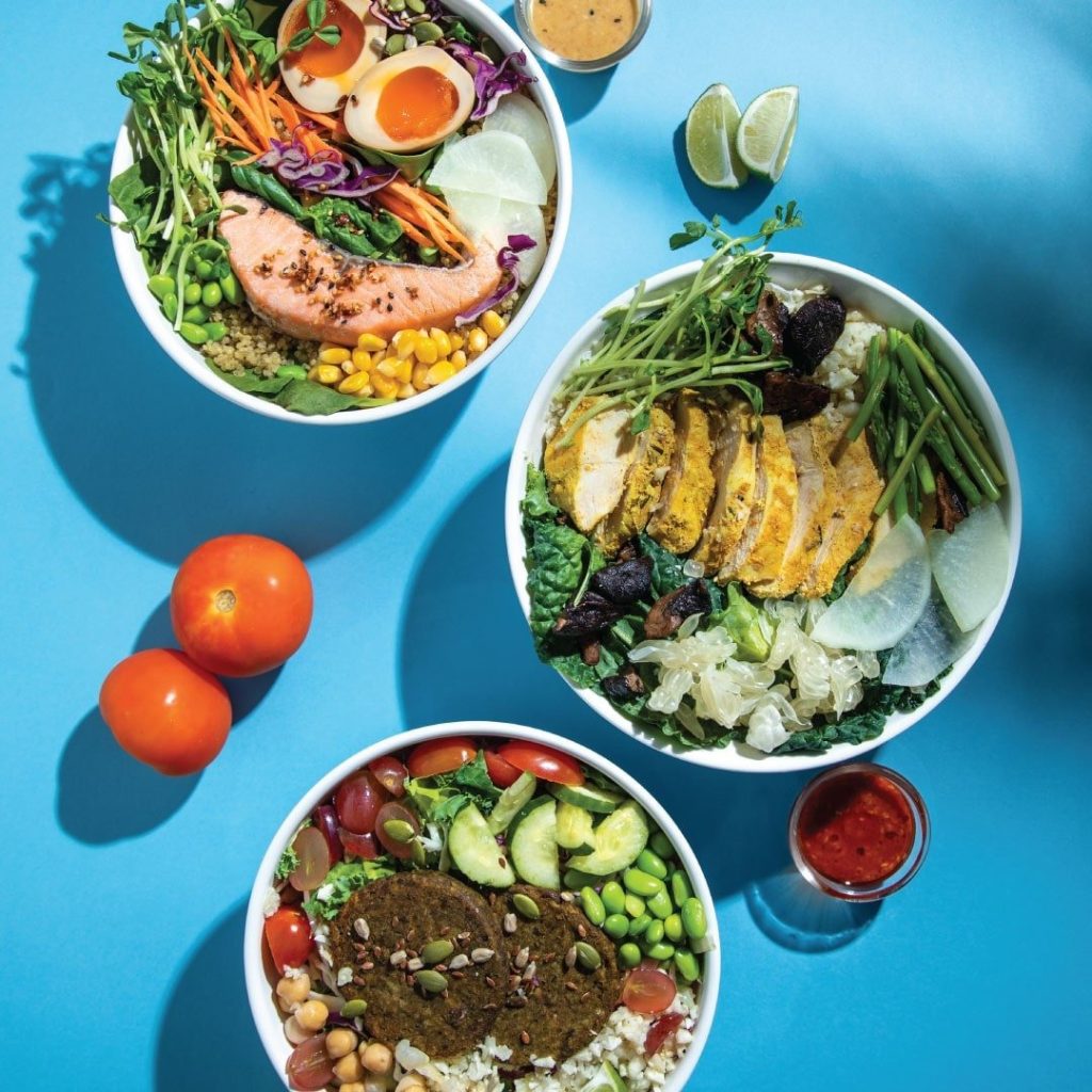 Overhead shot of three colorful and healthy SaladStop bowls on a bright blue background