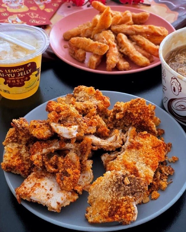 Close-up of a generous serving of Taiwanese-style fried chicken on a grey plate, with sweet potato fries, Lemon Ai-Yu Jelly drink, and noodles arranged around it.