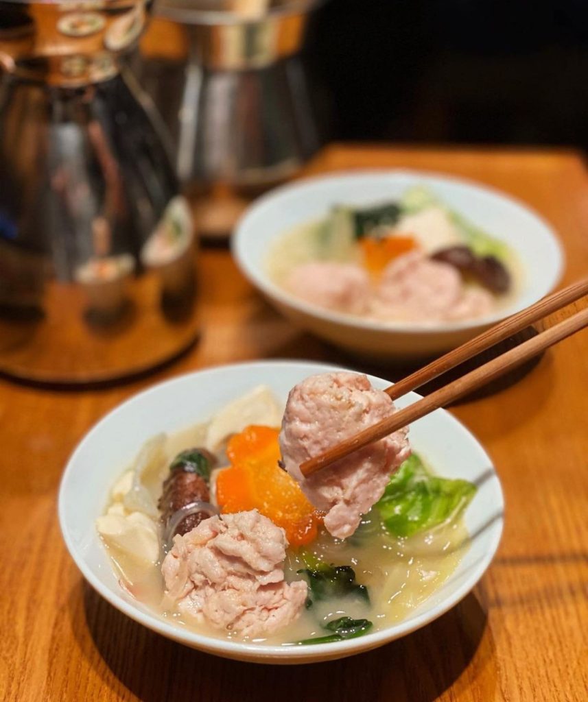 A bowl of Japanese meatball and vegetable soup (Nabe style), with chopsticks picking up a large meatball.