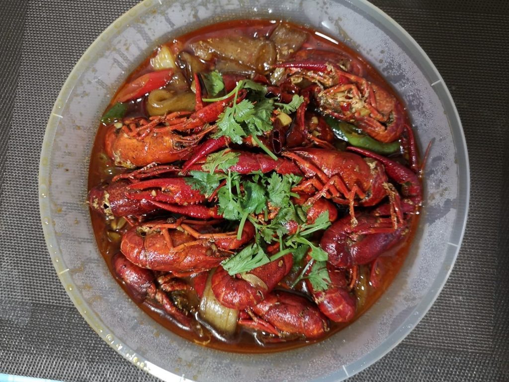 Bowl of spicy red crawfish cooked in a savory chili sauce with visible chili peppers and onions, topped with fresh cilantro