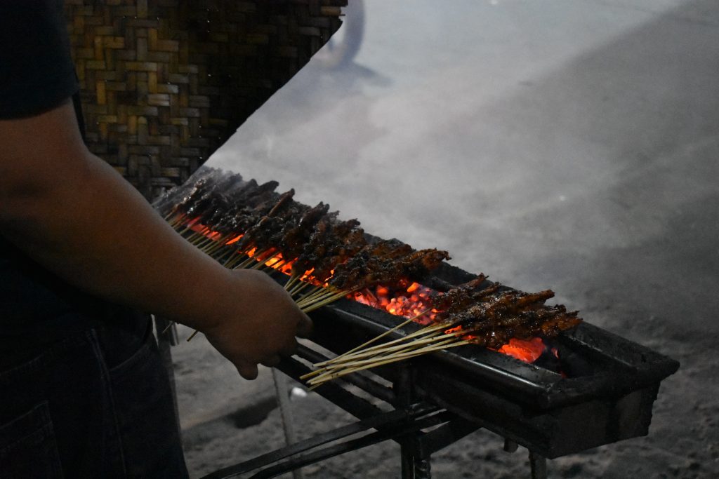 A person grilling skewers of meat over a charcoal grill