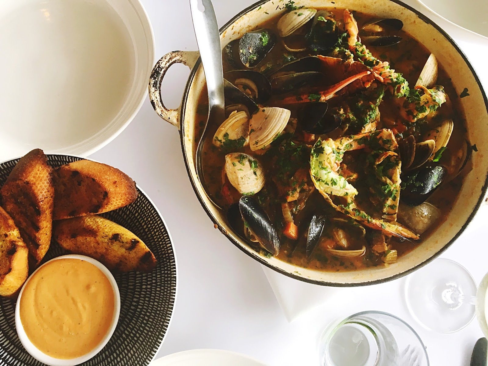 A large pot of French seafood stew, Bouillabaisse, served family-style with toasted bread and rouille sauce