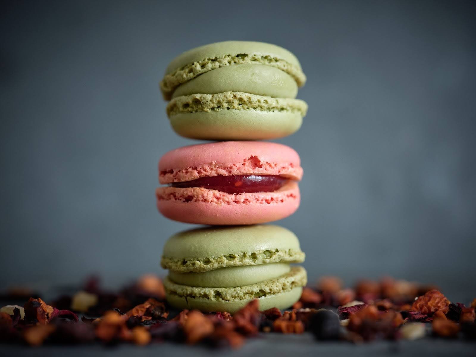 A stack of three colorful French macarons on a dark background