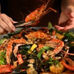 Hands reaching for a spread of dishes at the best halal seafood restaurant in Singapore