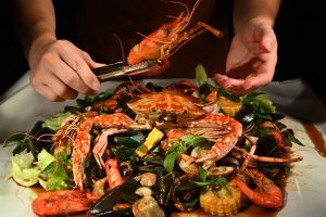 Hands reaching for a spread of dishes at the best halal seafood restaurant in Singapore